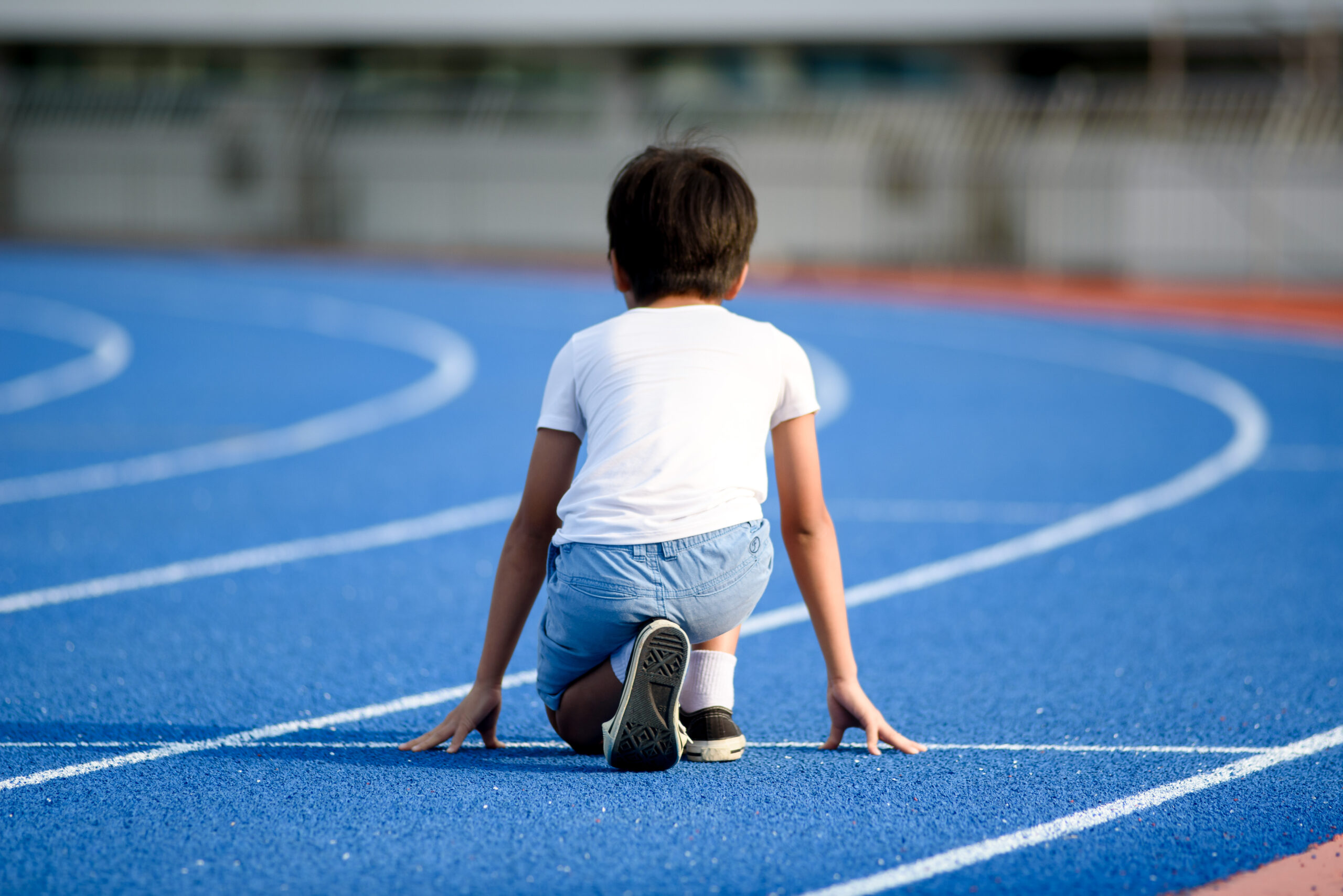 Young Asian boy prepare to start to run on a blue track in summer day